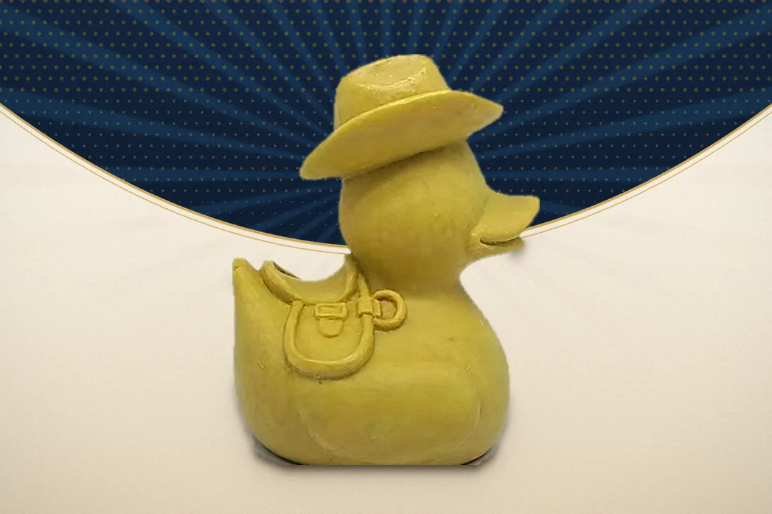 A hand-sculpted clay original of a cowboy duck with a wide-brim hat and a saddlebag, the first physical stage of a custom program before any tooling is cut